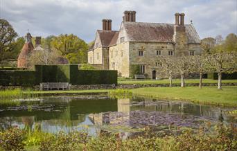 National Trust Bateman's House, pond in the foreground, surrounded by a bench, hedge and trees