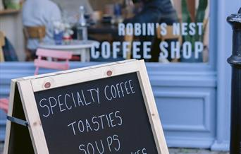 A sandwich board outside Robin's Nest Coffee Shop reads "Specialty coffee, toasties, soups, homemade cakes. Open 7.30 - 4 Monday to Friday, 10 - 4 Sat