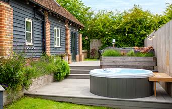 A bubbling hot tub on a deck, surrounded by planters with  lavender and herbs, next to a holiday cottage.