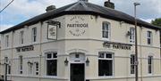 The outside of The Partridge pub showing a welcoming white painted building with dark roof