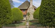 National Trust Alfriston Clergy House side view of house and chimney with paved area in the foreground and pruned trees
