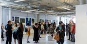 The BN9 Studio gallery space on the top floor of Newhaven's Marine Workshops. The gallery is busy with people visiting the Newhaven Open Call presente