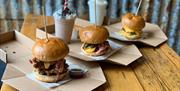 image of three burgers and 2 milkshakes, the burgers are stacked high with a skewer keeping them together with dipping sauces available.