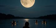 A computer generated image of people paddling at night under a full moon with LED lights around their boats