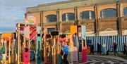 An outdoor view of Newhaven's Marine Workshops from The Sidings outdoor event space. The summer 2025 installation 'Free Form' by artists collective Le