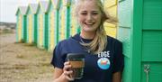 Smiling staff member from Edge by the Sea independent coffee shop infront of green and yellow beach huts in Littlehampton, Sussex|A selection of homem