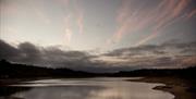 a dusk photo of the sun setting over the reservoir with clouds in the background