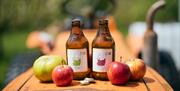 Bottles of cider with enticing drops of condensing water sit amongst apples on the bonnet of a rusty vintage orange kubota tractor on a sunny day.
