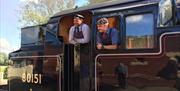 Bluebell Railway, Sheffield Park, exterior of engine number 80151 with two drivers leaning out the door and window, both wearing an apron, tie and pea