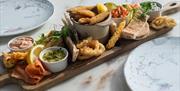 a seafood and dips platter - served on a wooden board. includes breaded whitebait, fried squid rings, salmon, pitta breads and a selection of dips