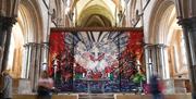 Inside Chichester Cathedral, an image showing the beams with a large artwork depicting an abstract cross in reds and white. Chichester cathedral