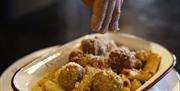 A comforting Italian pasta dish being finished with a generous sprinkle of grated parmesan. The plate features rigatoni pasta coated in rich tomato sa
