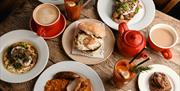 a birds eye views of a brunch meal with eggs and beans plate 1 and mushrooms and eggs on toast plate 2 with coffees and fresh drink
