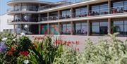 De La Warr Pavilion, Bexhill On Sea exterior, flowers in the foreground, visitors sitting on the outside balconies, the art exhibition and spiral stai