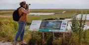 Bird watcher stood near the information board looking out over the nature reserve