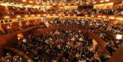 view of the auditorium of the Glyndebourne Opera House showing three balconies, a warm lit room with all seats filled