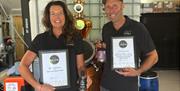 the proprietors holding up their awards with the distillery in the background