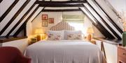 A cosy bedroom with double bed and quirky art work. exposed beams on ceiling and warm lighting