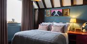 A cosy bedroom with double bed and quirky art work. exposed beams on ceiling and warm lighting