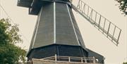 Picture of a black wooden smock windmill with white sweeps taken from behind