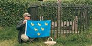 Man in cap and sunglasses in front of antique stocks holding the Sussex flag