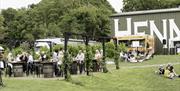 Out door seating with people sitting at tables and on the grass in front of the winery building