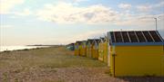 A curved row of beach huts on littlehampton beach with shingle and grass leading to the sea
