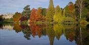 National Trust Sheffield Park, lake, reflection in the water of bank of trees in autumnal colours