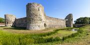 Pevensey Castle walls and round towers with field in the foreground