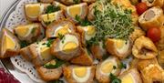 Platter of freshly made sausage rolls and sliced Scotch eggs served on a silver tray with garnish at Christina’s Tearoom, part of a traditional aftern