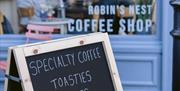 A sandwich board outside Robin's Nest Coffee Shop reads "Specialty coffee, toasties, soups, homemade cakes. Open 7.30 - 4 Monday to Friday, 10 - 4 Sat
