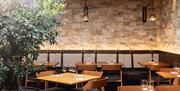 Inside the restaurant with wooden tables in the centre and cushioned bench seating along the walls.