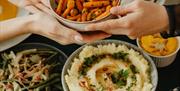 hands passing a dish of carrots across a range of bowls of food