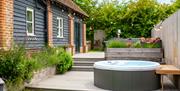 A bubbling hot tub on a deck, surrounded by planters with  lavender and herbs, next to a holiday cottage.