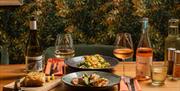 table with two plates of tasty looking food and white and rose wine glasses in the TERRA Courtyard at Tottington Manor