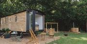 The Long View: a shepherd's hut style cabin with bifold doors opening onto a pretty paddock with outdoor dining deck, firepit, and woodfired hot tub