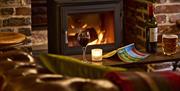 A glass of wine and beer on a table in front of a cosy log burner, next to a sofa at the Black Horse Climping