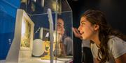 A young girl, approximately 10 years old, gazing in awe and wonder at a glass case display at The Novium Museum