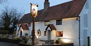 White exterior of the Black Horse in climping, with pub sign and patio furniture in front