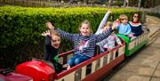 Children having fun and waving while riding the miniature train at Paradise Park