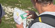 Image of the back of a persons head, they are looking at a map and compass with countryside in the background