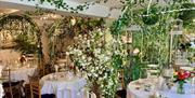 Interior of Christina’s Tearoom in Henfield, a beautiful indoor garden tearoom filled with flowers, ivy and vintage décor. Round tables are elegantly