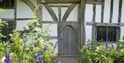 National Trust Alfriston Clergy House exterior wall with wooden door and beams, pathway bordered by flowering plants