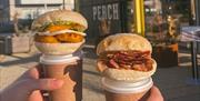 Two hands holding breakfast buns and coffees in from of the venue