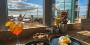 view of the beach from inside with a plate of loved and a cocktail on the bar table.