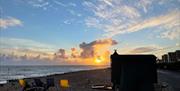 it is sunset on Worthing beach. There is a horsebox sauna, with deckchairs to the left of it.