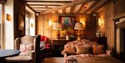 Cozy Room in The George In Rye, armchair and sofa with cushions, sideboard and maps underneath a ceiling with beams