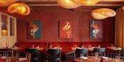 The George In Rye, dining room, tables laid for dining, paintings on the back wall above banquette seating, two oval tables in the foreground, wicker