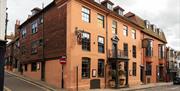 Exterior of The George In Rye, wrought iron balcony above entrance columns, and side hanging signs.