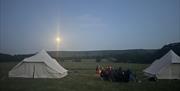 evening scene of campers sitting out side beside glamping tents